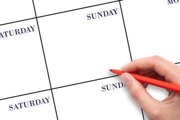 SUNDAY. Hand holding red pen writing in blank Sunday cell of a weekly calendar layout on clean white background, planning or scheduling concept. Save the date.