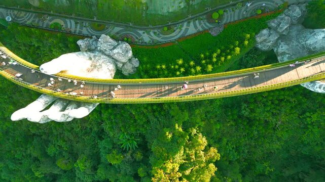 Aerial view of the Golden Bridge in Da Nang, Vietnam, held by a giant stone hand, surrounded by lush greenery.