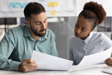 Serious customer showing documents to legal expert. Diverse couple of business colleagues reading paper reports together, doing paperwork, reviewing project business plan