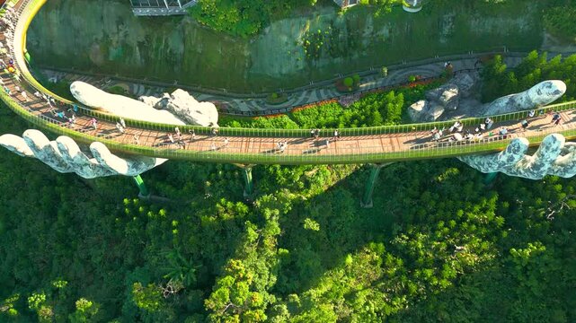 Aerial view of the Golden Bridge in Ba Na Hills, Vietnam, held by enormous hands against a lush green backdrop.