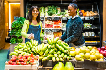 Saleswoman serving customer choosing bananas in organic supermarket