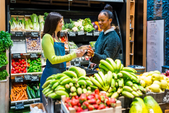 Saleswoman serving customer in organic supermarket with fresh produce