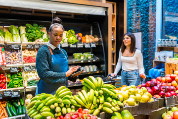 Saleswoman using digital tablet taking inventory of fresh produce in organic supermarket