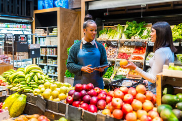 Saleswoman using tablet assisting customer choosing grapefruit in organic supermarket