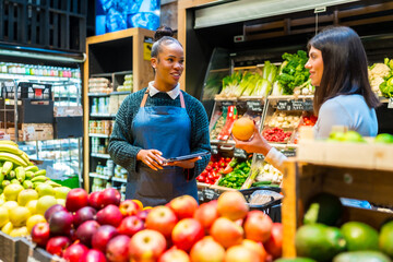 Saleswoman holding tablet assisting customer choosing grapefruit in organic supermarket