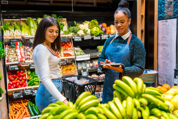 Saleswoman using digital tablet assisting customer choosing fresh produce in organic supermarket