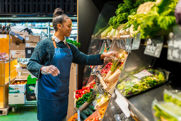 Saleswoman arranging fresh organic vegetables in supermarket