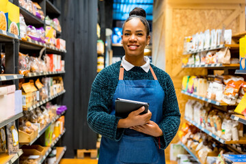Smiling saleswoman holding digital tablet, working in organic supermarket or grocery store