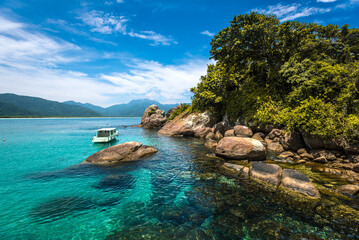 Fototapeta premium Crystal Clear Waters and Boat Near Rocky Shore in Angra dos Reis – Brazil