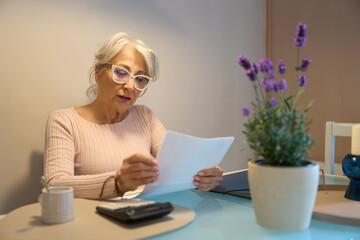 Senior woman carefully reviewing documents at home