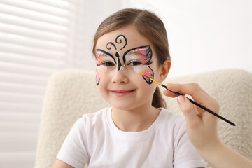 Animator drawing butterfly on girl's face indoors, closeup