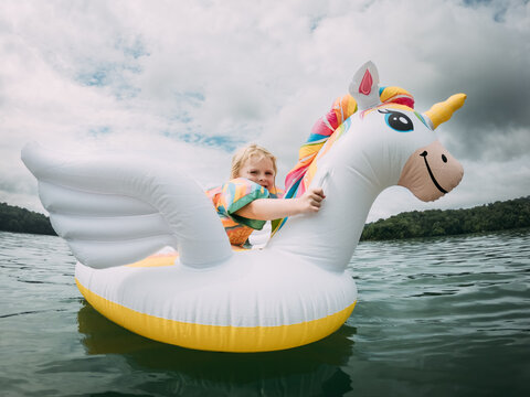 Young girl floating on a lake with a colorful unicorn inflatable