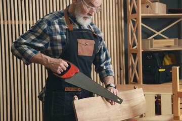 Relaxing hobby. Senior man working with wooden plank and saw in workshop