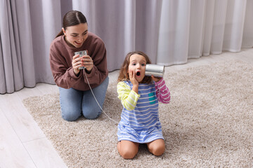 Woman and girl talking on tin can telephone indoors