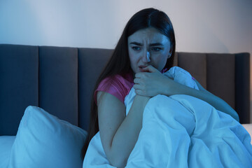 Fear of darkness. Scared young woman on bed in room at night