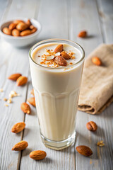 Almond milkshake topped with whole almonds and crushed nuts on a wooden background