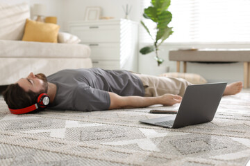 Man in headphones meditating near laptop on floor at home