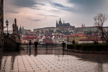 Obraz premium Panoramic view of Prague Castle and historic buildings along the Vltava River at dusk, with calm water and moody sky.