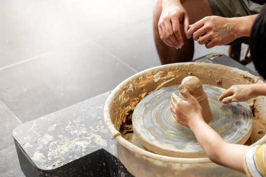 Making it together. Close-up of potter teaching child to make ceramic pot on the pottery wheel