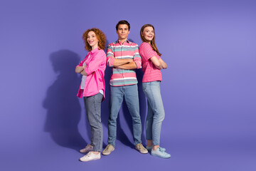 Obraz premium Three young friends posing together in casual outfits against purple background, showing unity and vibrant living