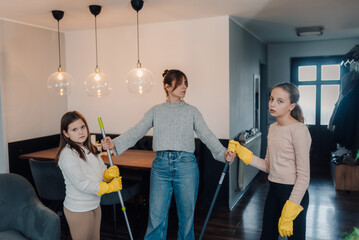 Mother and daughters cleaning floor together with mops in living room