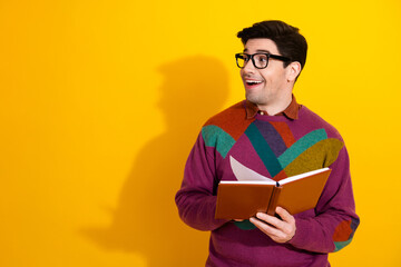 Smiling young man wearing a colorful sweater holding a book against a vibrant yellow background in a cheerful and lively pose
