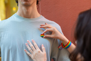 Woman placing rainbow heart pin on man's shirt, lgbtq plus support and pride