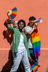 Young activists taking selfie and holding rainbow flag at gay pride parade