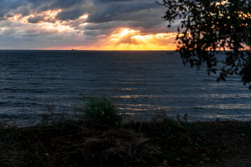 Gelendzhik resort. The sky is cloudy and the sun is setting. The sun is shining through the clouds, creating a beautiful orange and pink sky. The ocean is calm and the horizon is visible