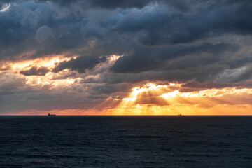 Gelendzhik resort. The sky is cloudy and the sun is setting. The sun is shining through the clouds, creating a beautiful orange and pink sky. The ocean is calm and the horizon is visible