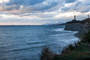 Gelendzhik resort. A lighthouse is visible on the shoreline of a body of water. The sky is cloudy and the water is calm
