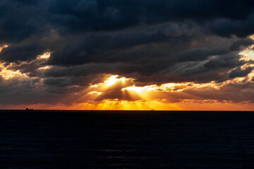 Gelendzhik resort. The sky is cloudy and the sun is setting. The sun is shining through the clouds, creating a beautiful orange and pink sky. The ocean is calm and the horizon is visible
