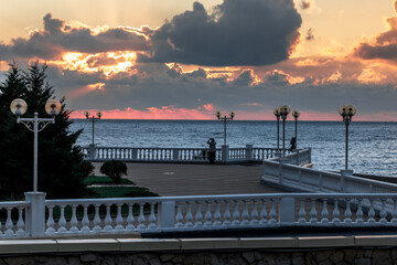 A beautiful sunset over the ocean with a pier in the background. The sky is filled with clouds and the water is calm. The pier is lit up with lights, creating a serene atmosphere