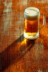 Bright golden beer in glass mug with soft foam placed on textured wooden surface in cozy bar. Top view photo. Concept of alcohol, festival, celebration, beer, culture, pub, bar.