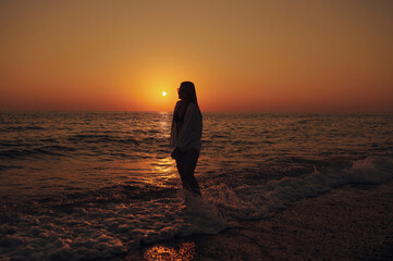Silhouette of woman at seaside, feeling tranquility and warmth of golden hour. Gentle surf, soft light, and scenic ocean view evoke peaceful escape. Perfect for vacation, meditation