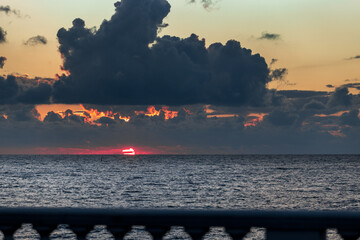 The sky is filled with clouds and the sun is setting. The water is calm and the sky is a beautiful orange color