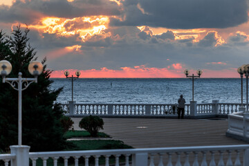 A beautiful sunset over the ocean with a pier in the background. The sky is filled with clouds and the water is calm. The pier is lit up with lights, creating a serene atmosphere