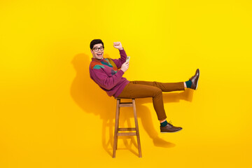 Cheerful young man in vibrant attire seated on a stool with an exciting pose, depicting a dynamic...