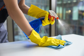 Young woman in yellow gloves cleaning the table in the office