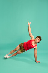 Young man performing side plank with raised arm, smiling confidently against mint studio...
