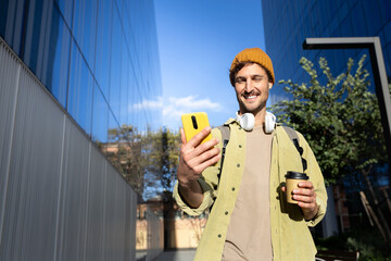 Happy man using mobile phone and drinking coffee in urban financial district. Copy space.