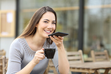 Happy woman in a bar terrace dictating message on phone