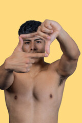 Fototapeta premium Shirtless man framing face with hands on yellow background
