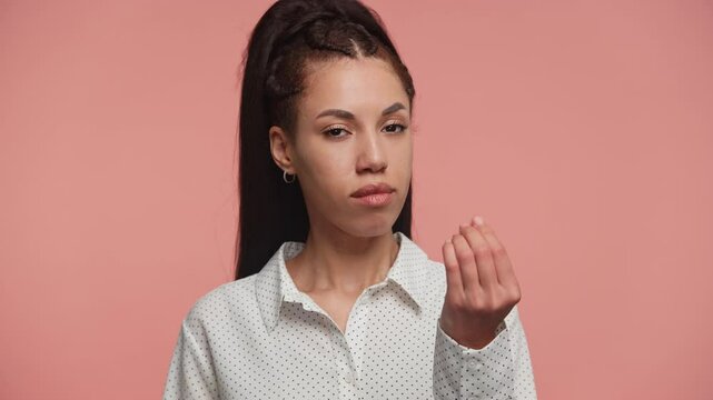 Serious woman making the money gesture on pink background
