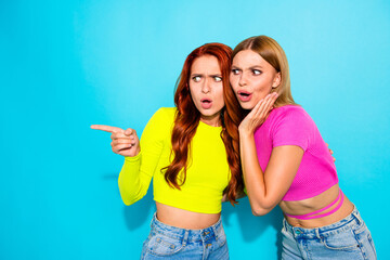 Stylish young girlfriends with contrasting hair colors sharing secrets against teal backdrop
