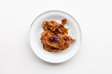 A batch of dried gelugur acid pieces isolated on a ceramic plate, ideal for food styling and traditional recipes.