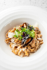 A gourmet pasta dish featuring fettuccine topped with mussels and garnished with fresh greens and grated cheese, presented elegantly in a white bowl