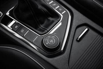 Driving modes selector in modern car. Automobile interior in dark tones, close-up view of bottom part of center console with automatic gear selector and driving controls.