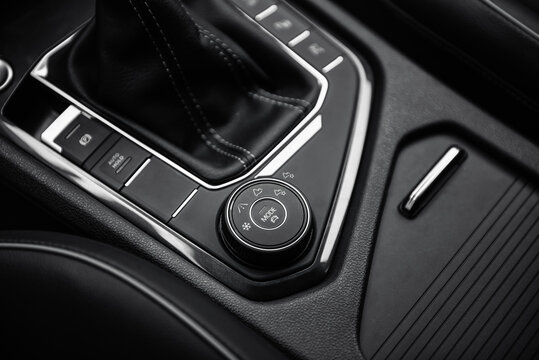 Driving modes selector in modern car. Automobile interior in dark tones, close-up view of bottom part of center console with automatic gear selector and driving controls.