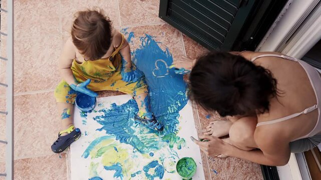 Young mother with her little boy mixing colors at hands yo leave beautiful handprints on the paper. Mother and child concept. Slowmotion. Mom amd child spend time together. Family, parenthood concept